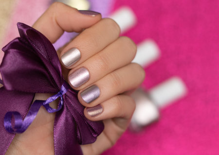 Female hand with pink nail design. Glitter pink nail polish manicure. Female model hand with perfect manicure hold purple bow tie on pink fabric background. Copy space.の写真素材