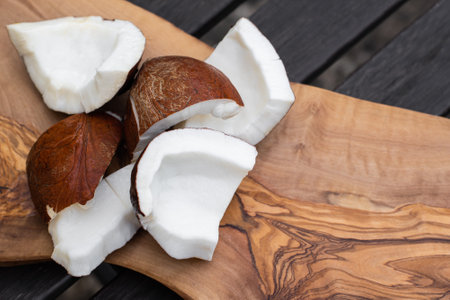Fresh coconut pieces on a wooden cutting board. Tasty shredded coconut on a desk. Tropical friut...
