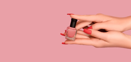Female hands with red nail design. Mate red nail polish manicure. Female model hands with perfect manicure hold red nail polish bottle on pale red background. Copy space. Place for text.の写真素材