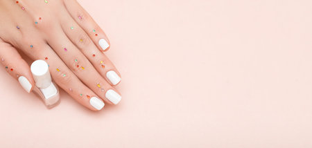 Female hand with white nail design. Glitter white nail polish manicure. Female model hand with perfect manicure hold white nail polish bottle on pink background. Copy space. Place for text.の写真素材
