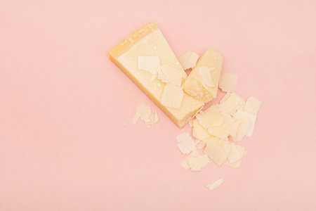 Cutted parmigiano reggiano or parmesan cheese on pink background. Delicious italian cheese -...