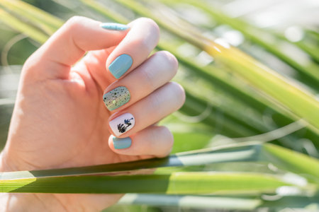 Female hand with vacation nail design. Glitter blue nail polish manicure with colorful abstract nail...