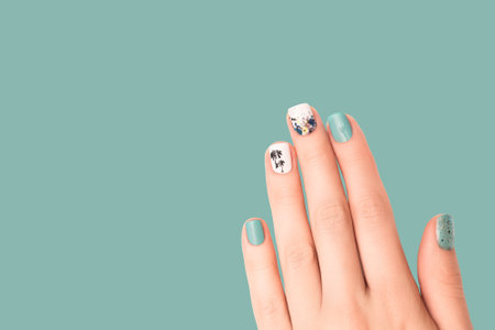 Female hand with vacation nail design. Glitter blue nail polish manicure with colorful abstract nail art. Female hand with perfect manicure and tropical sticker. Copy space. Place for text.の写真素材