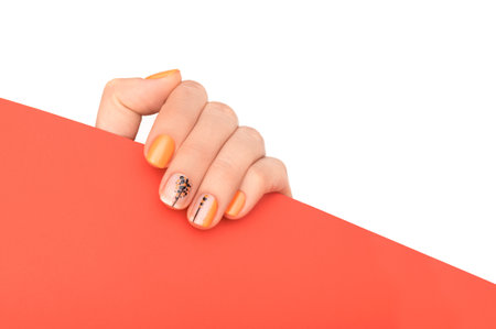 Female hand wih perfect orange manicure holding red paper corner on white background. Template for postcard, advertising banner or message. Nails card design element.の写真素材