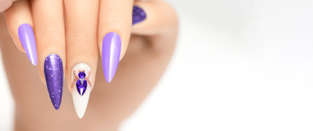 Female hand with stiletto nail design. Glitter purple nail polish manicure with purple rhinestones spider nail art. Female model hand on white background. Copy spaceの写真素材