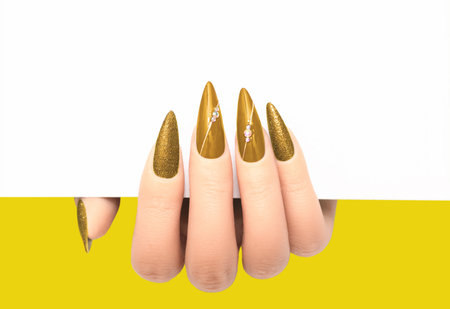 Female hand wih perfect gold stiletto manicure holding white paper on yellow background. Template for postcard, advertising banner or message. Nails card design element.の写真素材