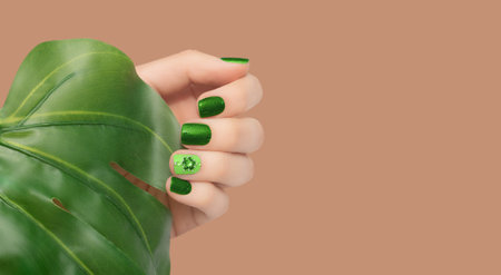 Female hand with vacation nail design. Glitter green nail polish manicure with rhinestone flower nail art. Female model hand with perfect green manicure on brown background. Copy space. Place for textの写真素材