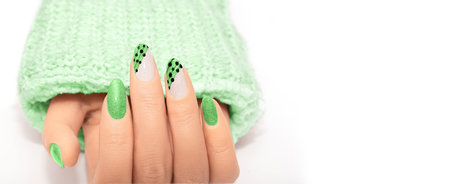 Female hand with green glitter nail design. Glitter green nail polish manicure with nail art. Female model hand in a green sweater with perfect manicure on white background. Advertising banners.の写真素材
