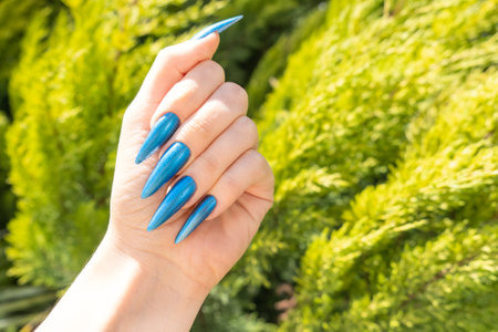 Female hand with summer nail design. Blue glitter nail polish manicure. Female hand with perfect nails on tropical background. Tropic manicure for postcard, poster or bannerの写真素材
