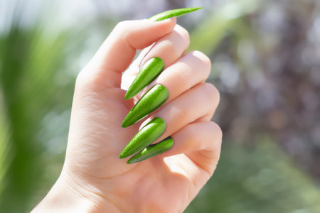 Female hand with summer nail design. Glitter green nail polish manicure. Female hand with perfect nails on tropical background. Tropic manicure for postcard, poster or bannerの写真素材