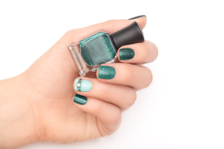 Female hand with colorful nail design. Glitter multi color manicure with nail art. Female hand with perfect manicure and navy rhinestones nail art hold navy nail polish bottle.の写真素材