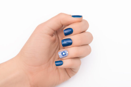 Female hand with classic nail design. Glitter blue nail polish manicure with rhinestone flower nail art. Female model hand with perfect blue manicure on white background. Copy space. Place for textの写真素材
