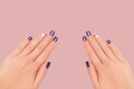 Female hands with purple nail design. Glitter purple nail polish manicure with rhinestones nail art. Female model hands with perfect purple manicure on orange background. Copy space. Place for text.の写真素材