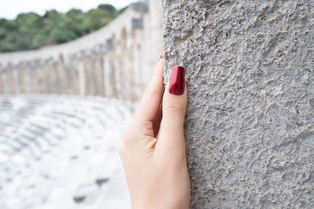 Female hand with pink long nail design at sunny day. Glitter red nail polish summer manicure. Female model hand with perfect red manicure in an old ruins. Tropical vacation manicure.の写真素材