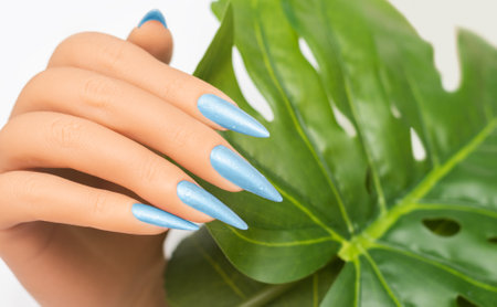 Female hand with stiletto nail design. Blue glitter nail polish manicure. Female hand with perfect manicure on white backgroundの写真素材