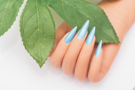 Female hand with stiletto nail design. Blue glitter nail polish manicure. Female hand with perfect manicure on white backgroundの写真素材