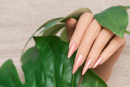 Female hand with long nails with glitter nail polish. Long Pink Nail Designs. Woman hand with pink manicure on wooden background.の写真素材