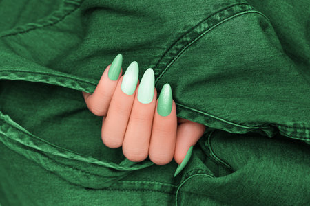 Female hand with glitter nail polish. Green nail design with two shades. Women hand with sparkle manicure on green denim backgroundの写真素材
