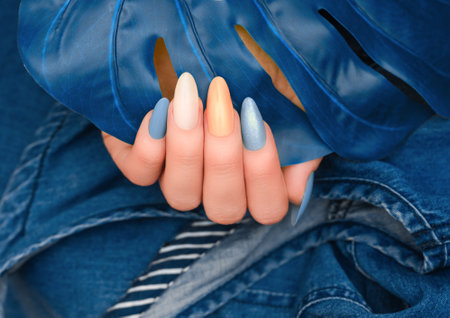 Female hand with glitter nail polish. Blue nail design with two shades. Women hand with sparkle manicure on blue denim backgroundの写真素材