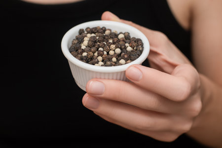 Bowl filled with natural aromatic Black and White pepper in female hand. White small bowl with spices.の写真素材
