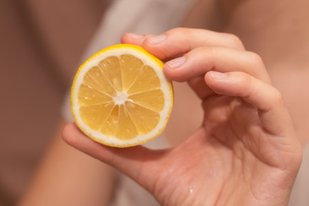 Hand Showcasing Half a Lemon. A person's fingers displaying a bright lemon halfの写真素材