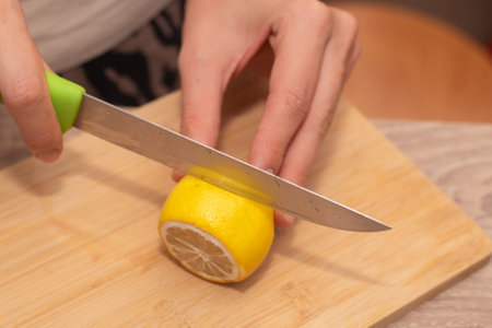 Cutting a Fresh Lemon on a Wooden Board. Hand slicing a yellow lemon on a bamboo cutting boardの写真素材