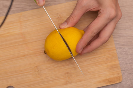 Cutting a Fresh Lemon on a Wooden Board. Hand slicing a yellow lemon on a bamboo cutting boardの写真素材
