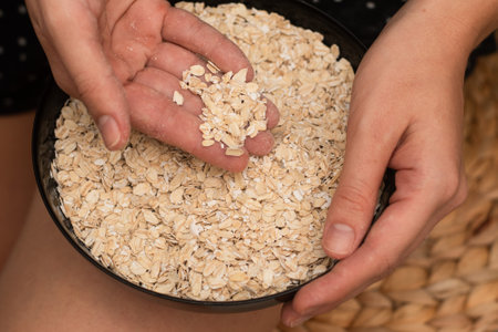 Oats Trickling from Hand into Bowl. Hand sprinkling rolled oats into a black bowlの写真素材