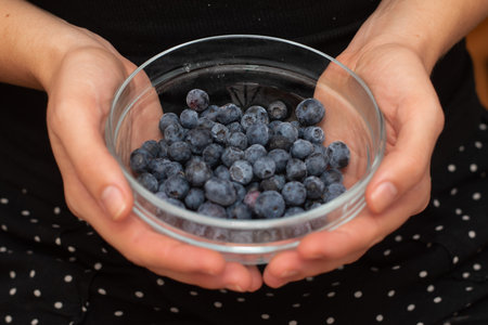 Fresh Blueberries in a Glass Bowl in Female Handsの写真素材