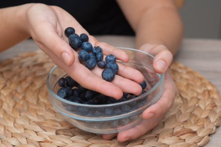 Fresh Blueberries in a Glass Bowl in Female Hands. Picking ripe blueberries from a glass bowlの写真素材