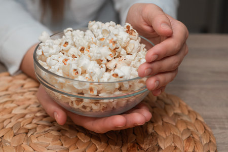Woman Holding Bowl of Fresh Popcorn. Close-up of a woman's hands holding a transparent bowl filled...