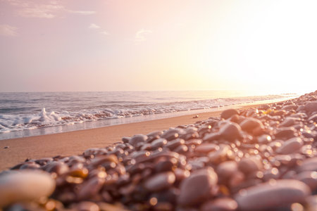 Golden Sunrise Over Pebble Beach. Warm sunrise illuminating a pebble-covered beach with gentle waves, casting a serene glow on the shorelineの写真素材