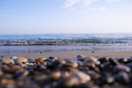 Warm sunrise illuminating a pebble-covered beach with gentle waves, casting a serene glow on the...