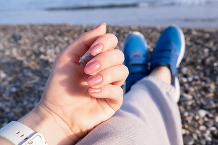 Hand with Pink Glitter Nail Polish Relaxing at the Beach. Close-up of a hand with pink glitter nail polishの写真素材