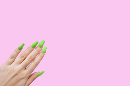 Green Nail Polish on Female Hand with Long Nails. Female hand with long, green nail polish on a pink backgroundの写真素材