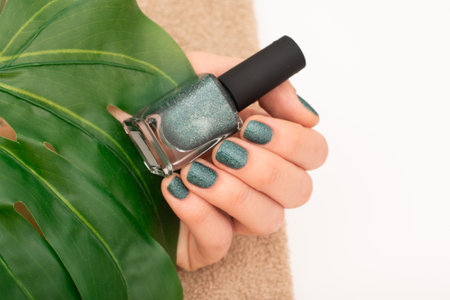 Green Glitter Nail Polish on Female Hand and leaf on background. Close-up of a hand with green...
