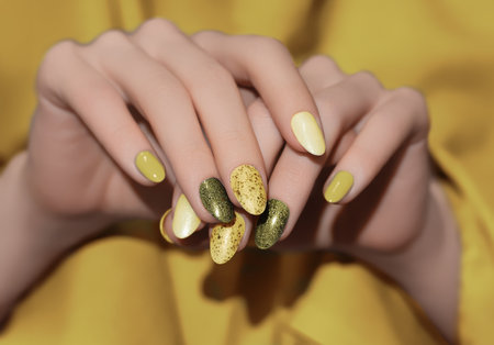 Female hands with yellow nail design. Glitter nail polish manicure. Woman hands on yellow fabric background.の写真素材