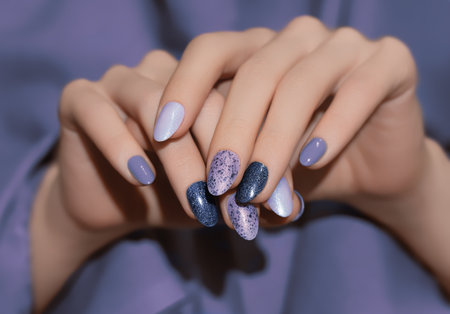 Female hands with purple nail design. Glitter nail polish manicure. Woman hands on purple fabric background.の写真素材
