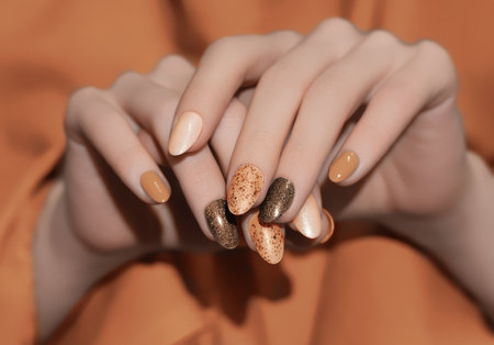Female hands with orange nail design. Glitter nail polish manicure. Woman hands on orange fabric background.の写真素材
