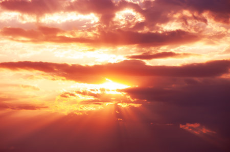 A dramatic sunset with glowing orange and pink light rays breaking through clouds, creating a stunning sky scene.の写真素材