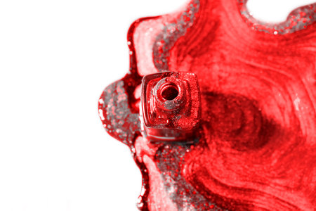 An open bottle of red glitter nail polish spilled on a white surface, creating a swirling, shiny pattern.の写真素材
