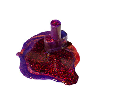 A bottle of purple and red glitter nail polish spilled on a white surface, forming a vibrant and sparkling puddle.の写真素材