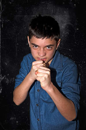 Aggressive boy.Bad caucasian teenager ready for a boxing fight on a dark black-gray background.の写真素材