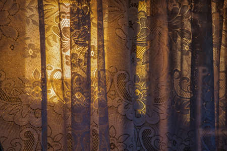 Floral lace curtains background texture.Old lace curtains on the window of a boat with sunset light through themの写真素材
