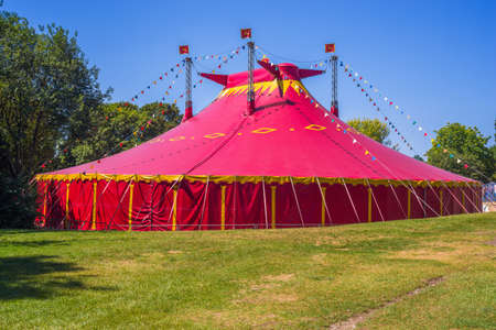 Circus tent on a green field. Red circus tent in green built in a green field against a blue sky.の写真素材