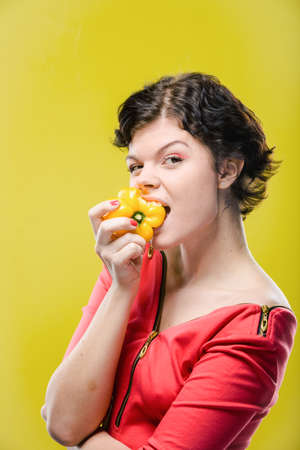 Girl is eating yellow pepper on colored background. Natural unretouched image.の写真素材