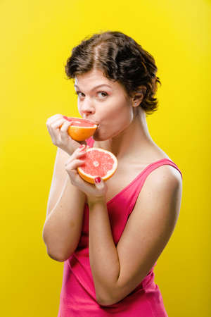 Girl with sliced red grapefruit on colored background. Natural unretouched image.の写真素材