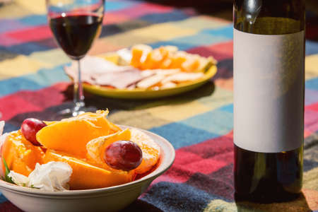 Served table with wine bottle, orange and grape covered with colored blanketの写真素材