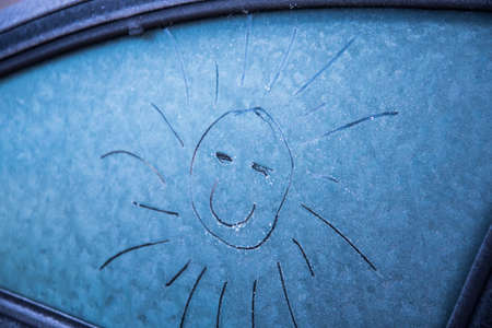 The sun is painted on the frozen glass of the car. The sun smilesの写真素材
