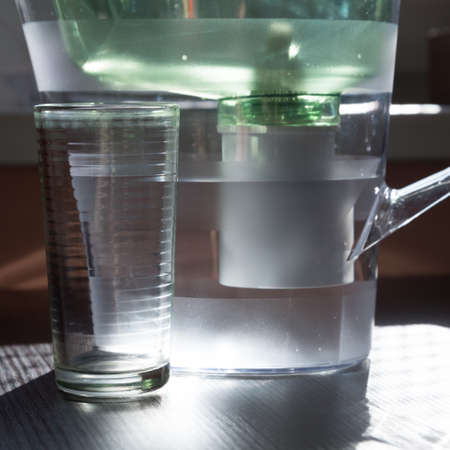 Close-up of a jug with a water purification cartridge. A stream of clear water flows from the...